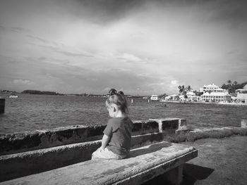 Girl sitting on bench by sea