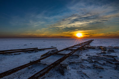 Rusty railroad track on desert against sky during sunset