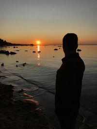 Silhouette man looking at sea against sky during sunset