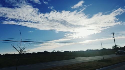 Electricity pylons on landscape against cloudy sky