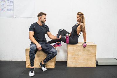 Full length of young couple sitting against wall