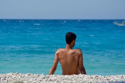 Rear view of shirtless man at beach against sky