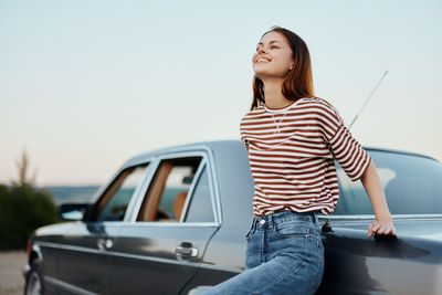 Portrait of young woman standing against car