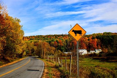 Road sign by trees against sky