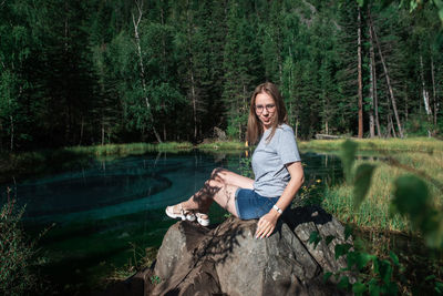 Portrait of smiling woman sitting by lake in forest