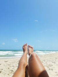 Low section of woman legs on beach against blue sky