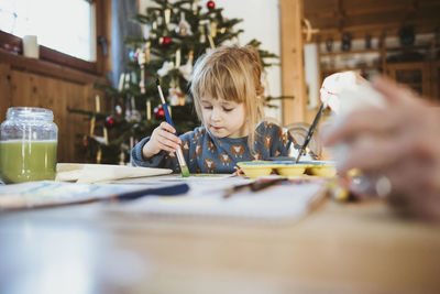 Girl painting on paper at home during christmas