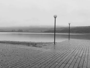 Street light on footpath by lake against sky