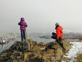 Rear view of people on rock against sky during winter