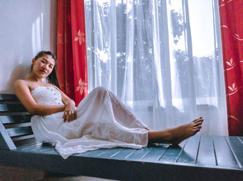 Portrait of young woman sitting by window at home