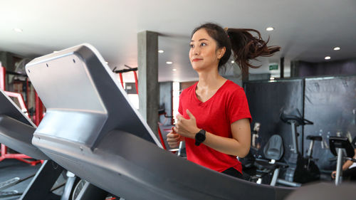 Smiling young woman running on treadmill in gym