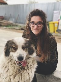 Portrait of young woman with dog sitting on retaining wall