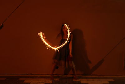 Blurred motion of woman holding illuminated sparkler against wall at night