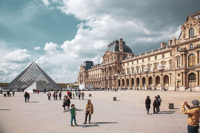 Group of people in front of building against cloudy sky