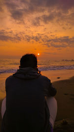Rear view of man looking at sea against sky during sunset