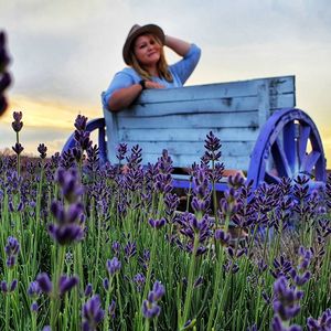 Portrait of young woman standing amidst purple flowering plants on field