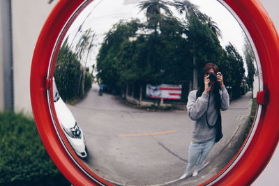 Reflection of man photographing on side-view mirror