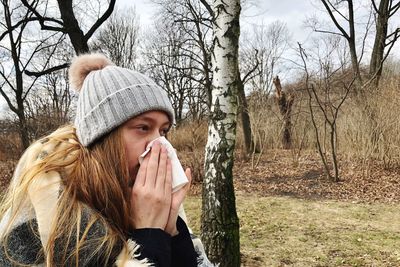 Close-up of teenage girl blowing nose while standing in forest