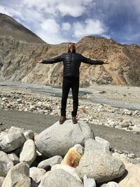 Man with arms outstretched standing on stone against mountains