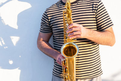 Midsection of man playing saxophone against wall
