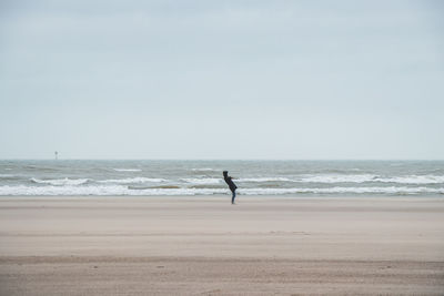 Side view of woman walking at beach against sky