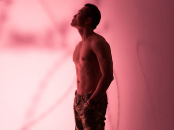 Side view of shirtless man standing against pink background