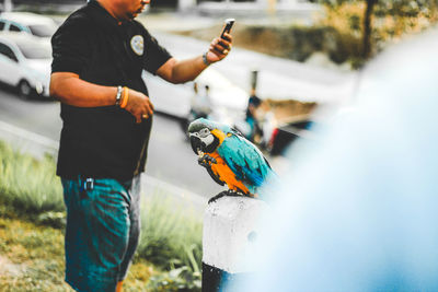 Midsection of man using mobile phone by bird outdoors