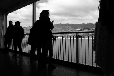 Silhouette woman standing on railing by sea against sky