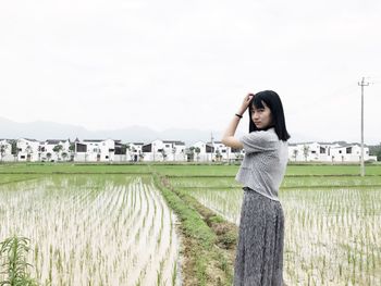 Portrait of young woman standing in farm against clear sky