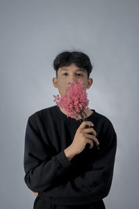 Portrait of young man with flower against gray background