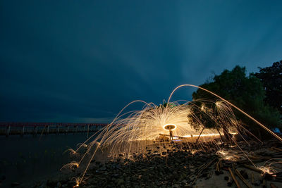 Man spinning wire wool while standing at beach against sky at night