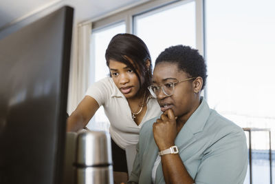 Female programmer discussing with colleague over computer in office