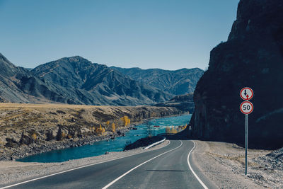 Road sign by mountains against clear sky