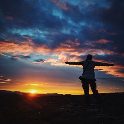 Silhouette of woman standing against sky at sunset