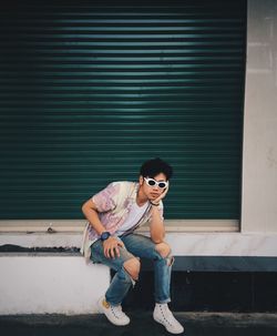 Portrait of man sitting against closed green shutter