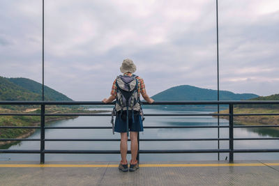 Rear view of woman standing on bridge over lake against sky