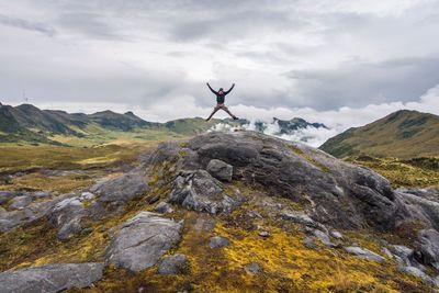 Man with arms outstretched on rock against sky