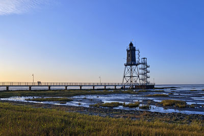 Lighthouse by sea against clear sky