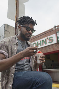 A young man sitting and eating frozen yoghurt.