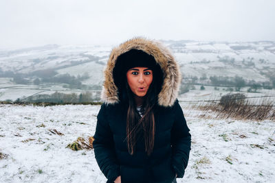 Portrait of surprised beautiful woman standing on snow field against sky