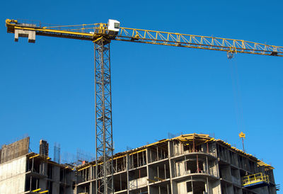 Low angle view of crane against clear blue sky