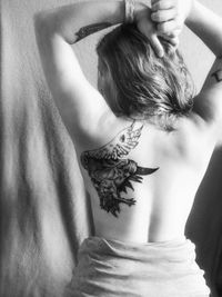 Rear view of shirtless woman with hand in hair showing tattoo