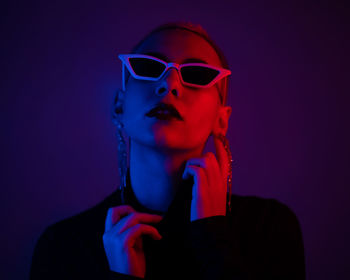 Portrait of young woman holding sunglasses against colored background