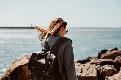 Rear view of woman wearing backpack while standing on pier over sea against clear sky