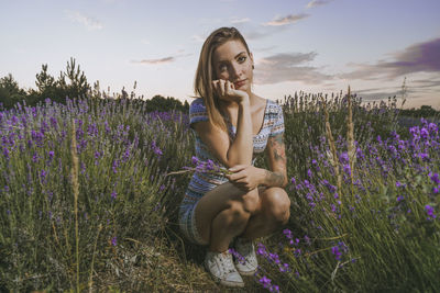 Young woman standing by purple flowers on field against sky