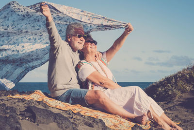 Couple sitting on beach against sky