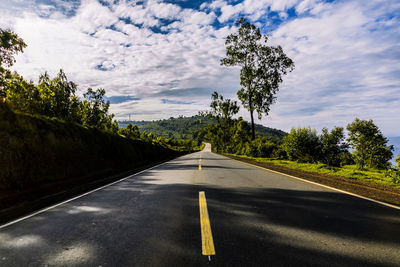 Empty road along trees and against sky