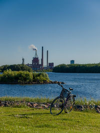 Bicycle by river in city against sky