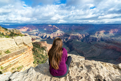 Rear view of woman sitting on rock against sky