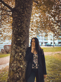 Woman smoking cigarette while standing by tree